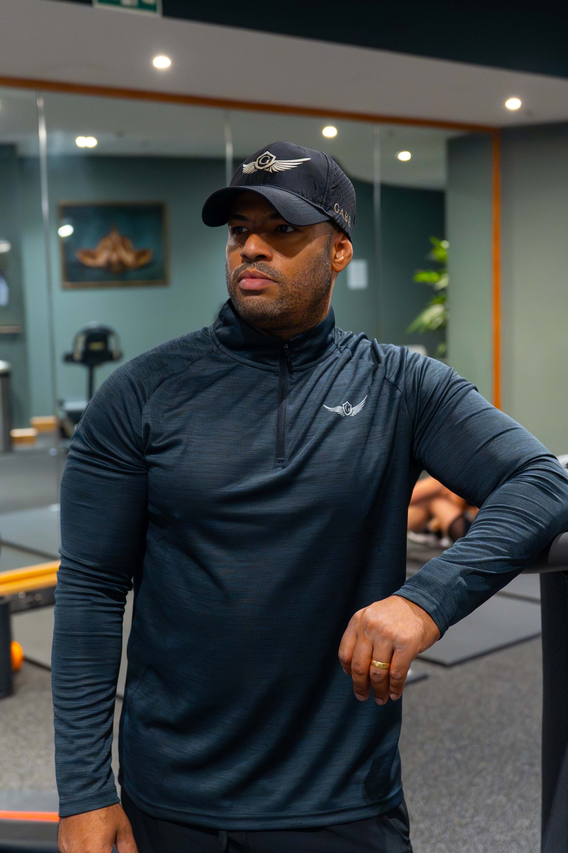 Man wearing black athletic outfit and cap in a gym setting