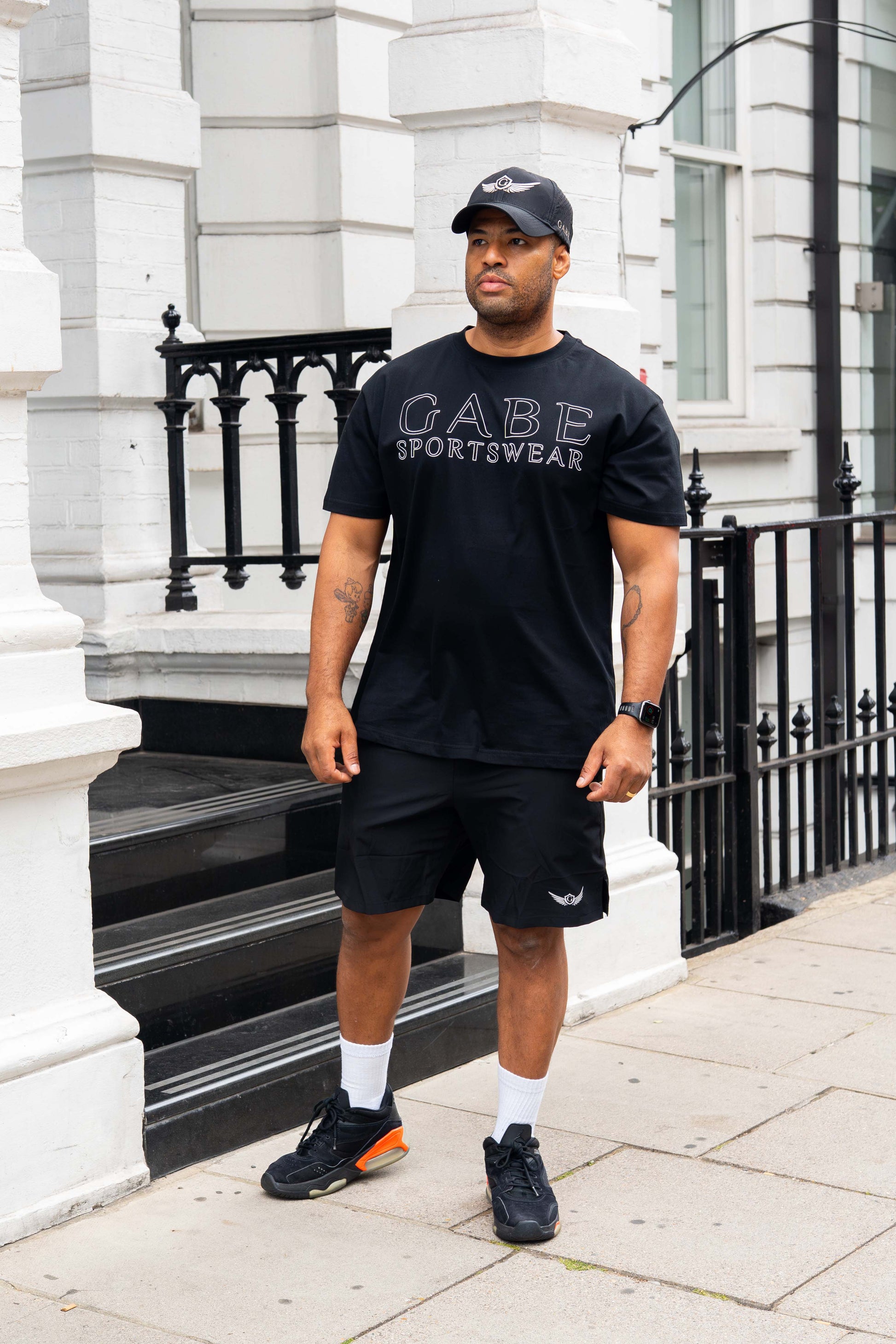 Man wearing a black 'GABE Sportswear' t-shirt standing on a city street.