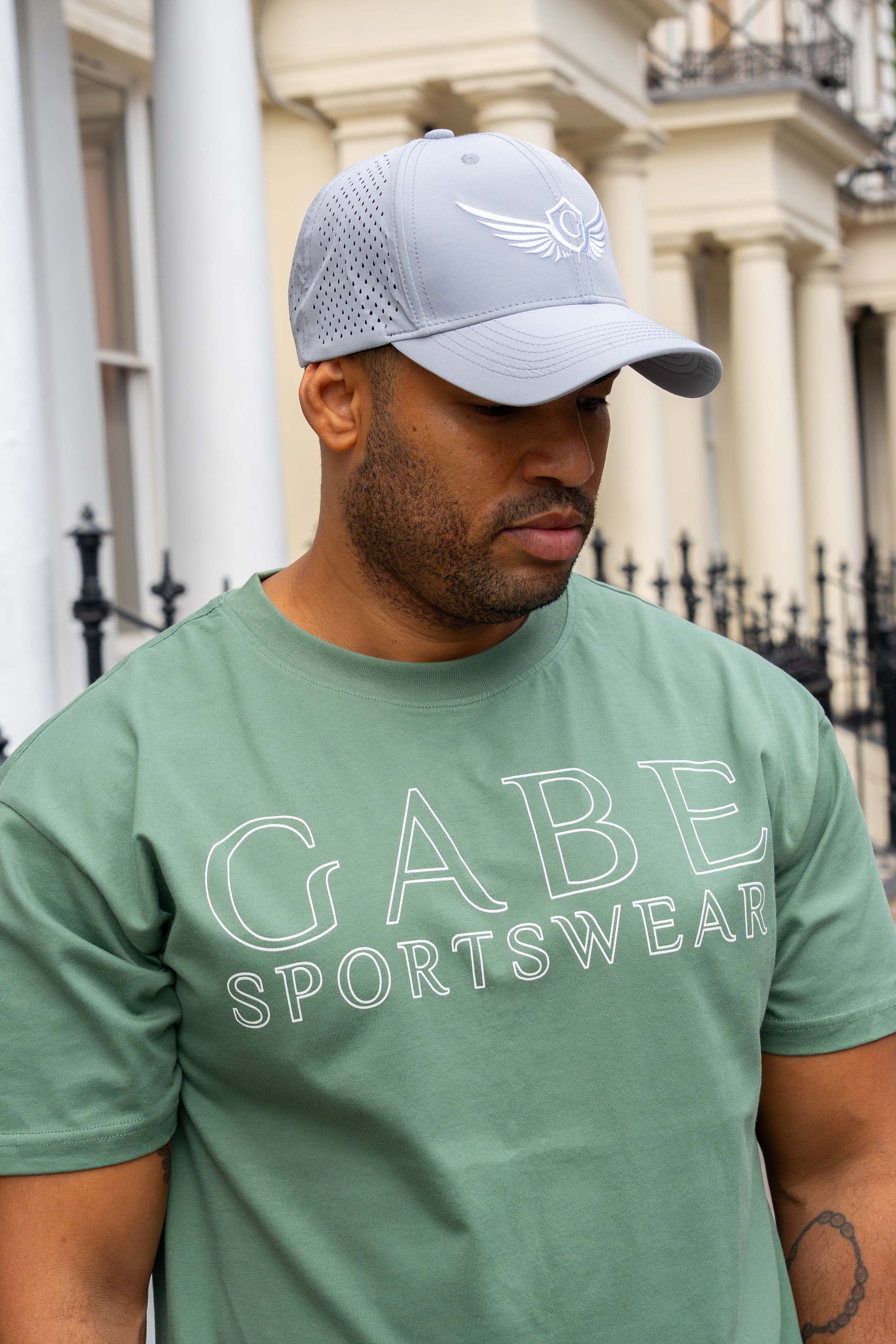 Man wearing a green 'Gabe Sportswear' t-shirt and grey cap outdoors.
