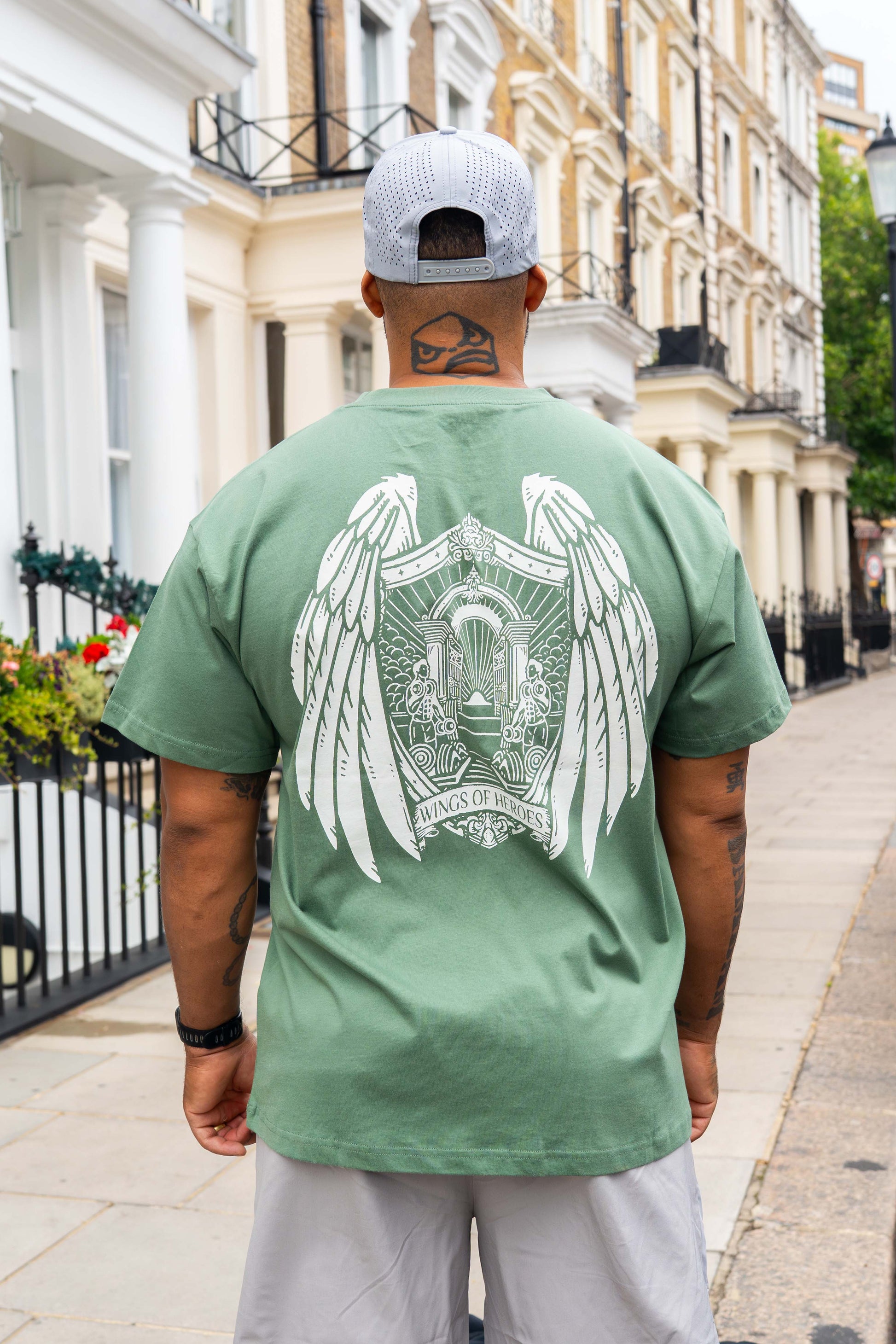 Man wearing a green t-shirt with a white graphic design on the back, standing on a street.