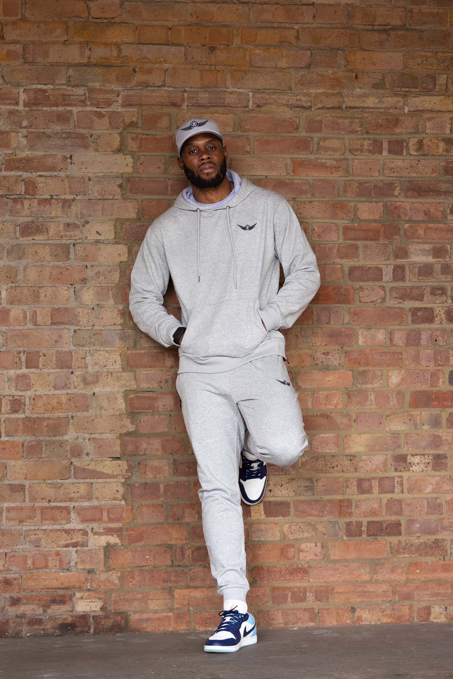 Man wearing a gray tracksuit leaning against a brick wall