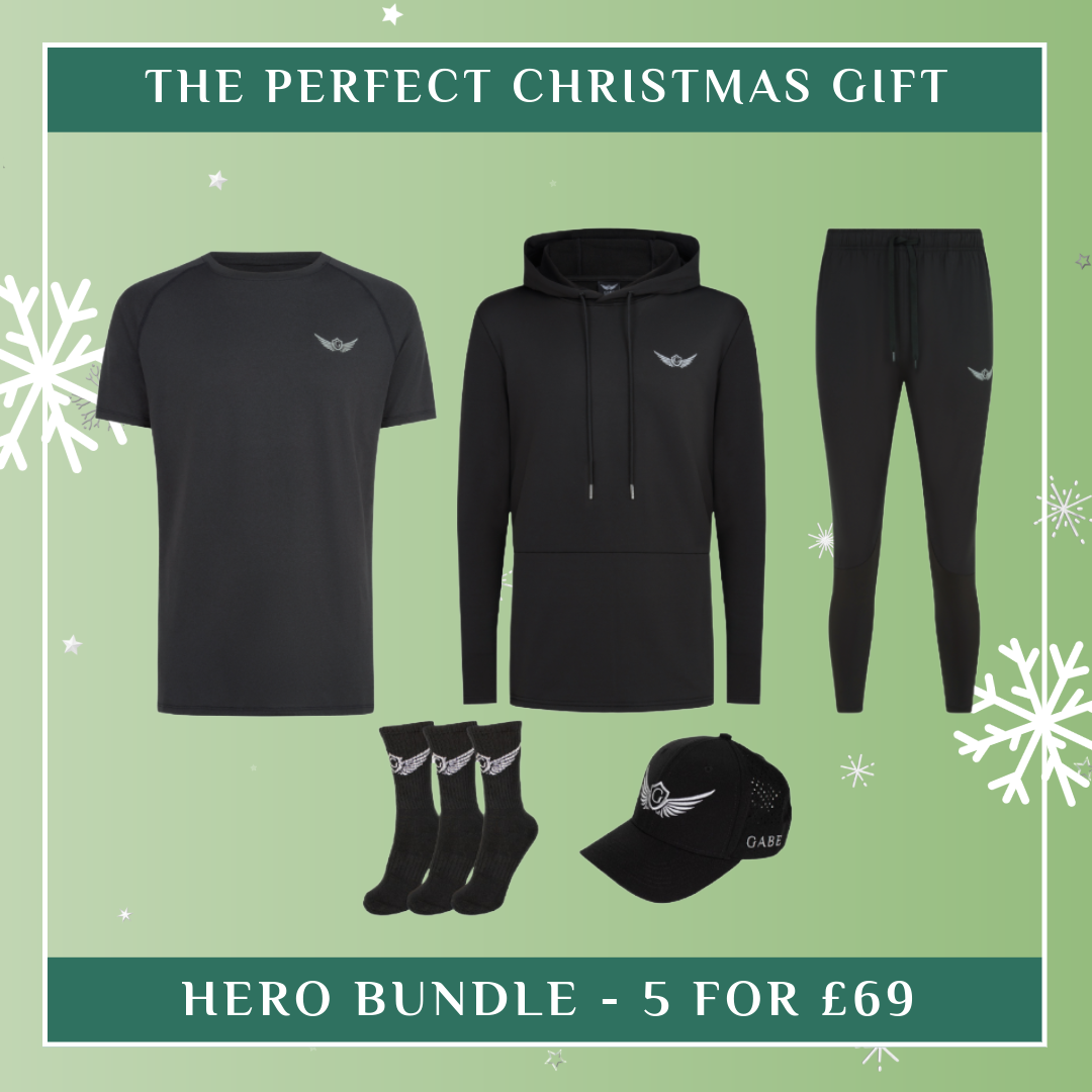 Black clothing bundle with t-shirt, hoodie, pants, socks, and cap on a green background with text 'The Perfect Christmas Gift'.