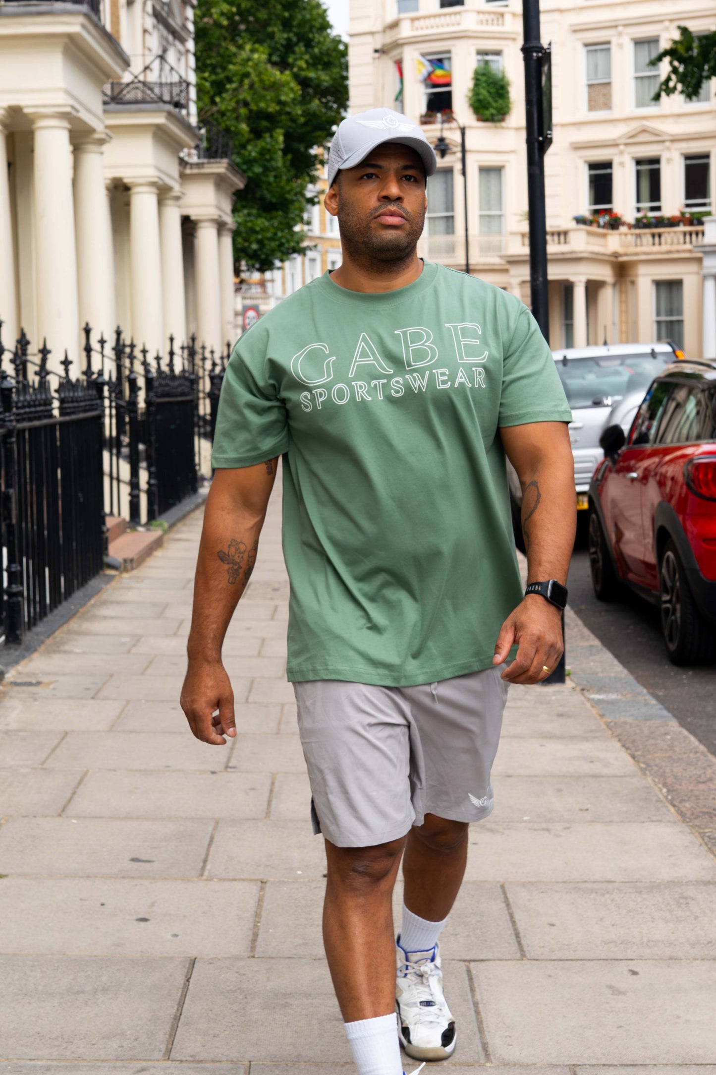 Man walking on a sidewalk wearing a green t-shirt with 'GABE SPORTSWEAR' text.